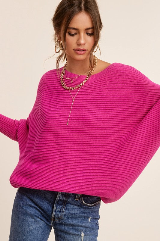 Person wearing a Mae Sweater, a loose-fitting, off-the-shoulder, hot pink ribbed knit with bubble sleeves, paired with blue jeans, gold hoop earrings, and a gold chain necklace.