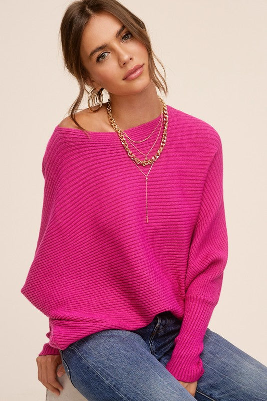 Person wearing a Mae Sweater, a loose-fitting, off-the-shoulder, hot pink ribbed knit with bubble sleeves, paired with blue jeans, gold hoop earrings, and a gold chain necklace.