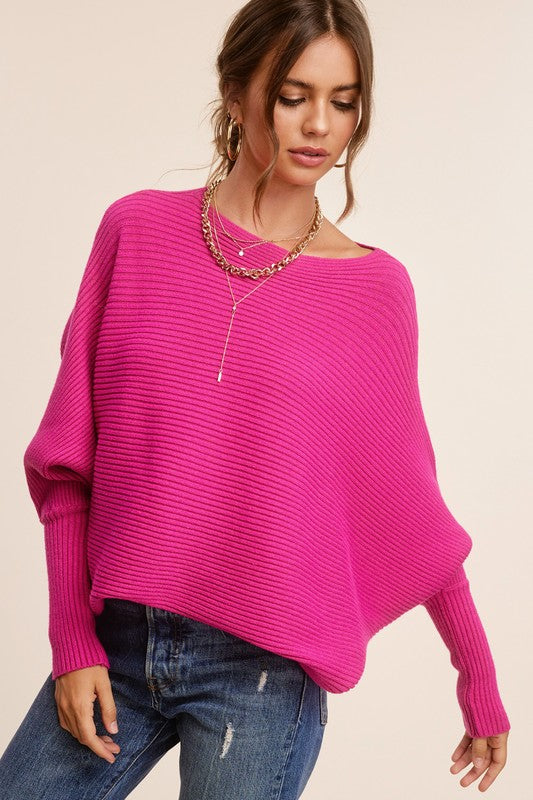 Person wearing a Mae Sweater, a loose-fitting, off-the-shoulder, hot pink ribbed knit with bubble sleeves, paired with blue jeans, gold hoop earrings, and a gold chain necklace.