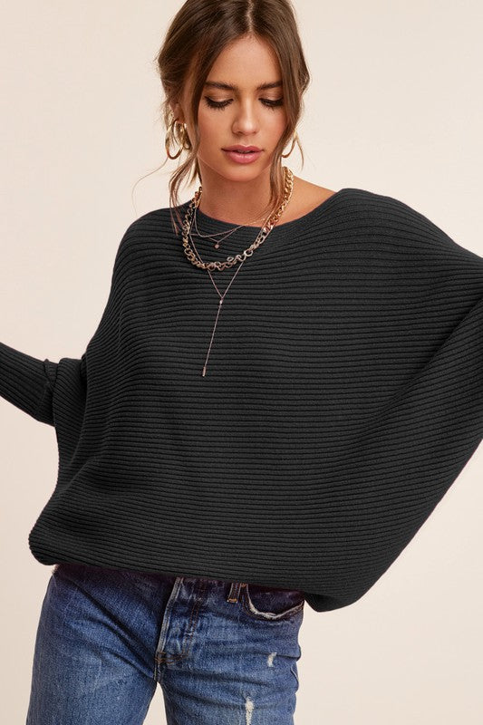 Person wearing a Mae Sweater, a loose-fitting, off-the-shoulder, hot pink ribbed knit with bubble sleeves, paired with blue jeans, gold hoop earrings, and a gold chain necklace.