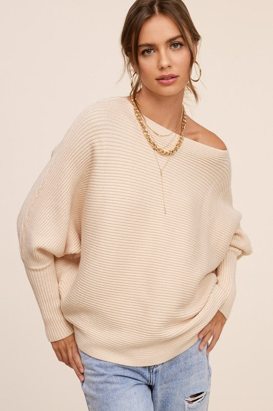 Person wearing a Mae Sweater, a loose-fitting, off-the-shoulder, hot pink ribbed knit with bubble sleeves, paired with blue jeans, gold hoop earrings, and a gold chain necklace.