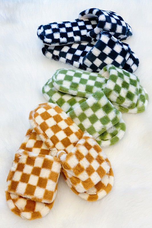 Four pairs of Luxe Lounge Checker Cozy Slippers in colors black, green, and tan are arranged on a white fluffy surface. Each pair boasts non-slip soles and a soft fabric construction for ultimate comfort.