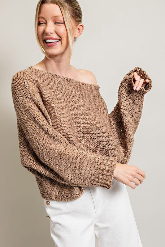 A woman smiles while wearing the Loose Fit Knit Top featuring a boat neckline, paired with white pants with button embellishments on the side. She stands against a plain background.