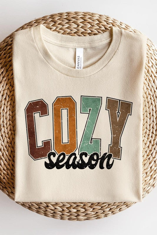 An "UNISEX SHORT SLEEVE" orange graphic tee hangs on a hanger, showcasing the words "COZY season" in a vibrant and bold font. This 100% cotton creation is perfect for anyone looking to embrace comfort and style.