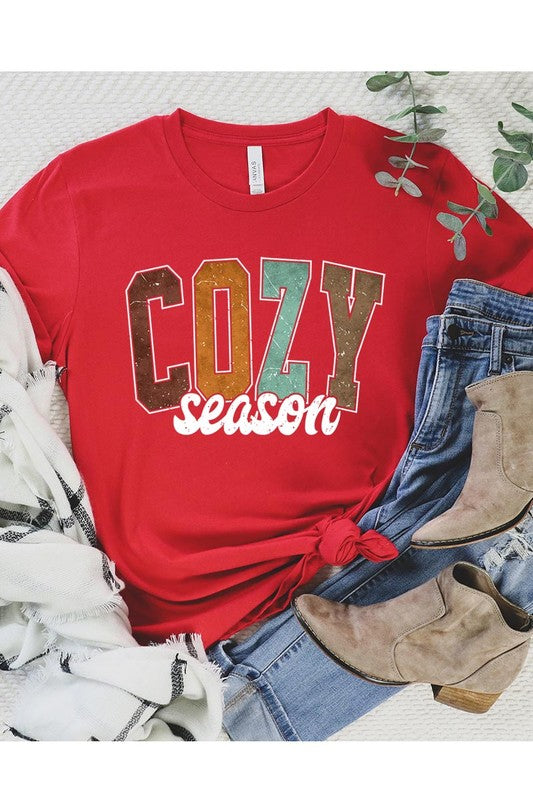 An "UNISEX SHORT SLEEVE" orange graphic tee hangs on a hanger, showcasing the words "COZY season" in a vibrant and bold font. This 100% cotton creation is perfect for anyone looking to embrace comfort and style.