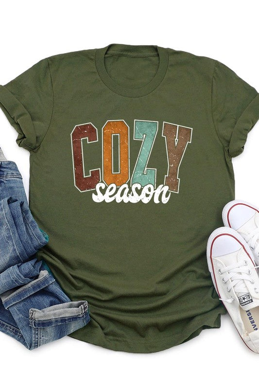 An "UNISEX SHORT SLEEVE" orange graphic tee hangs on a hanger, showcasing the words "COZY season" in a vibrant and bold font. This 100% cotton creation is perfect for anyone looking to embrace comfort and style.