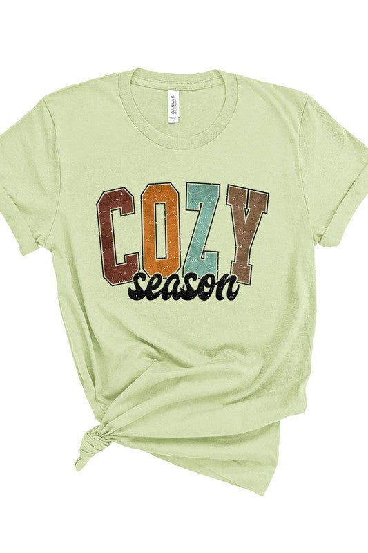 An "UNISEX SHORT SLEEVE" orange graphic tee hangs on a hanger, showcasing the words "COZY season" in a vibrant and bold font. This 100% cotton creation is perfect for anyone looking to embrace comfort and style.