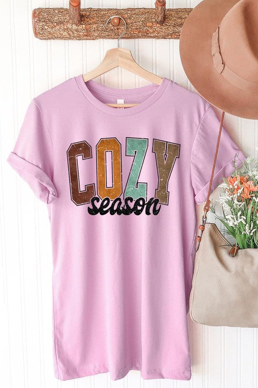 An "UNISEX SHORT SLEEVE" orange graphic tee hangs on a hanger, showcasing the words "COZY season" in a vibrant and bold font. This 100% cotton creation is perfect for anyone looking to embrace comfort and style.