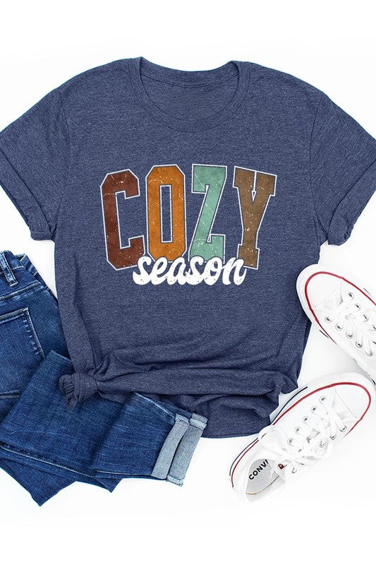 An "UNISEX SHORT SLEEVE" orange graphic tee hangs on a hanger, showcasing the words "COZY season" in a vibrant and bold font. This 100% cotton creation is perfect for anyone looking to embrace comfort and style.