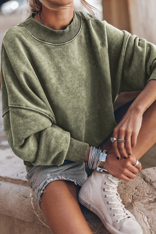 A person wearing a Mineral Washed Acid dye Sweatshirt Pullover with a drop shoulder design and distressed denim shorts stands with hands in pockets.