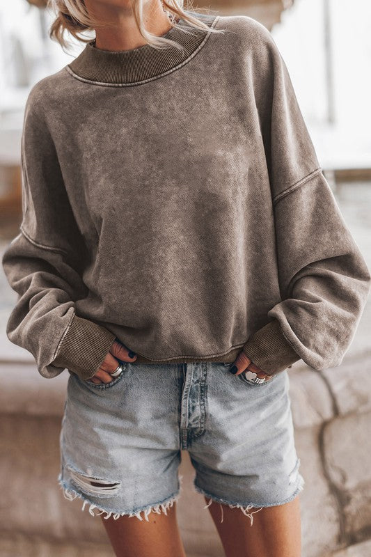 A person wearing a Mineral Washed Acid dye Sweatshirt Pullover with a drop shoulder design and distressed denim shorts stands with hands in pockets.