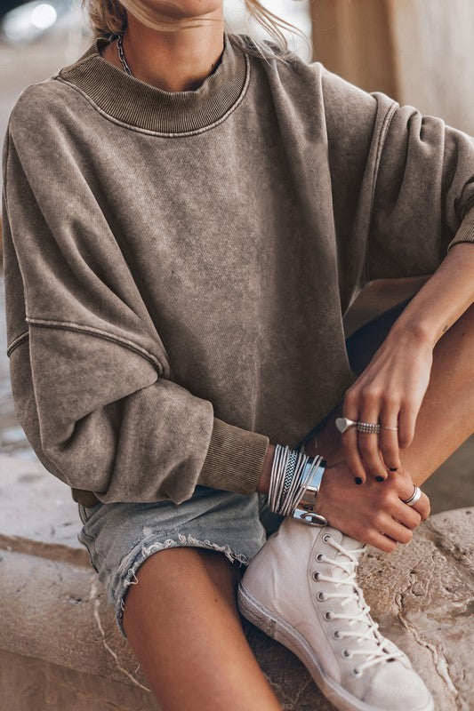 A person wearing a Mineral Washed Acid dye Sweatshirt Pullover with a drop shoulder design and distressed denim shorts stands with hands in pockets.