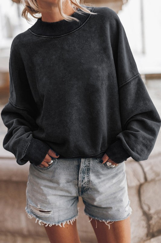A person wearing a Mineral Washed Acid dye Sweatshirt Pullover with a drop shoulder design and distressed denim shorts stands with hands in pockets.