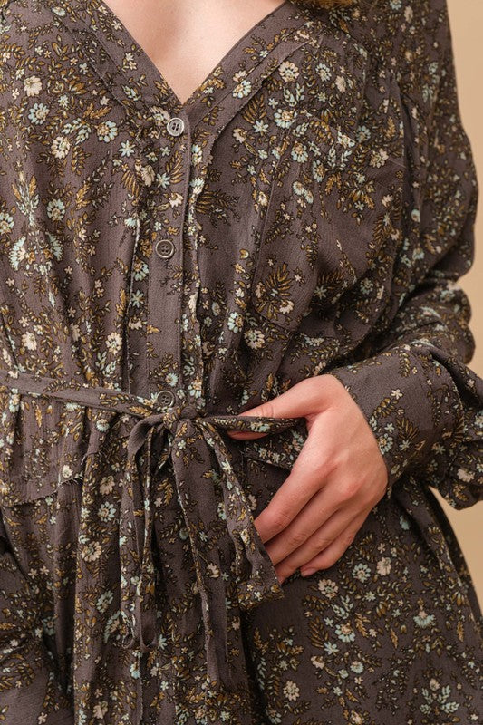 A person stands against a beige background, wearing a cowboy hat, a belt, cowboy boots, and the Rayon Crinkle Ditsy Floral Raw Shift Shirt Dress in gray.