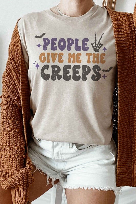 Person wearing a white, 100% cotton People Give Me The Creeps Graphic Tee with colorful, playful font text "People Give Me The Creeps" and graphic elements like a bat and skeleton hand.