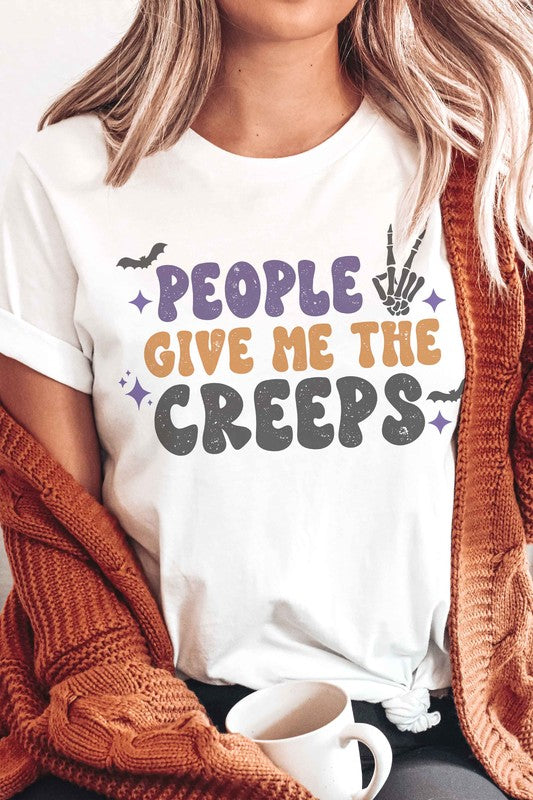 Person wearing a white, 100% cotton People Give Me The Creeps Graphic Tee with colorful, playful font text "People Give Me The Creeps" and graphic elements like a bat and skeleton hand.