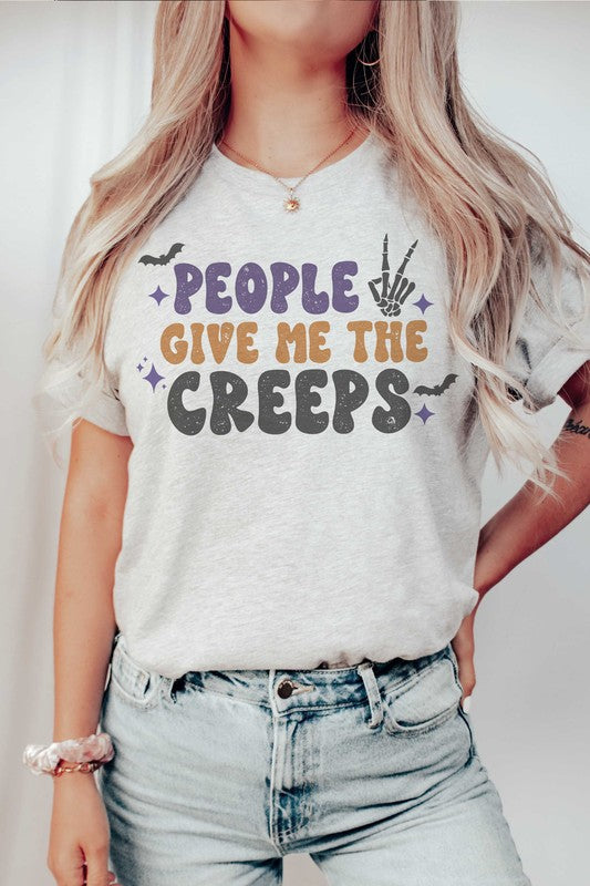 Person wearing a white, 100% cotton People Give Me The Creeps Graphic Tee with colorful, playful font text "People Give Me The Creeps" and graphic elements like a bat and skeleton hand.