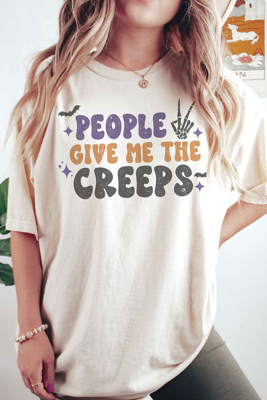 Person wearing a white, 100% cotton People Give Me The Creeps Graphic Tee with colorful, playful font text "People Give Me The Creeps" and graphic elements like a bat and skeleton hand.