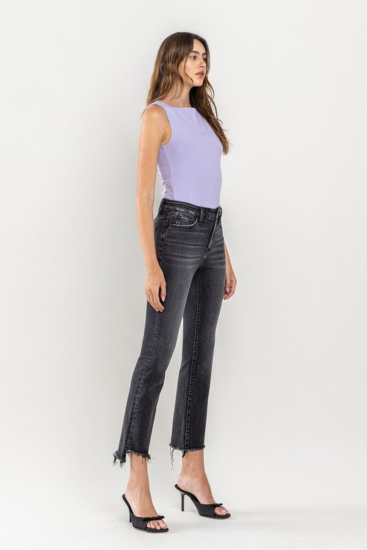 A person wearing High Rise Raw Step Hem Crop Flare Jeans in dark gray and black heeled sandals, standing against a light background.