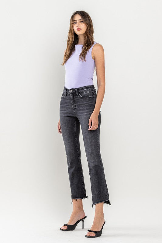 A person wearing High Rise Raw Step Hem Crop Flare Jeans in dark gray and black heeled sandals, standing against a light background.