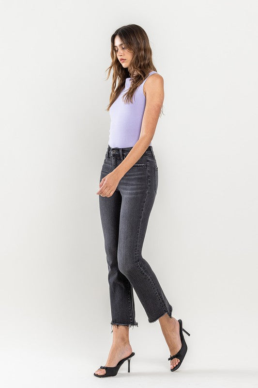 A person wearing High Rise Raw Step Hem Crop Flare Jeans in dark gray and black heeled sandals, standing against a light background.