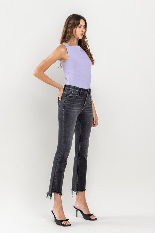 A person wearing High Rise Raw Step Hem Crop Flare Jeans in dark gray and black heeled sandals, standing against a light background.