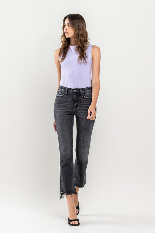 A person wearing High Rise Raw Step Hem Crop Flare Jeans in dark gray and black heeled sandals, standing against a light background.