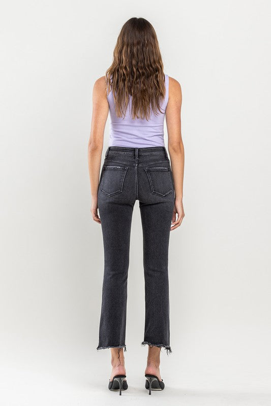 A person wearing High Rise Raw Step Hem Crop Flare Jeans in dark gray and black heeled sandals, standing against a light background.