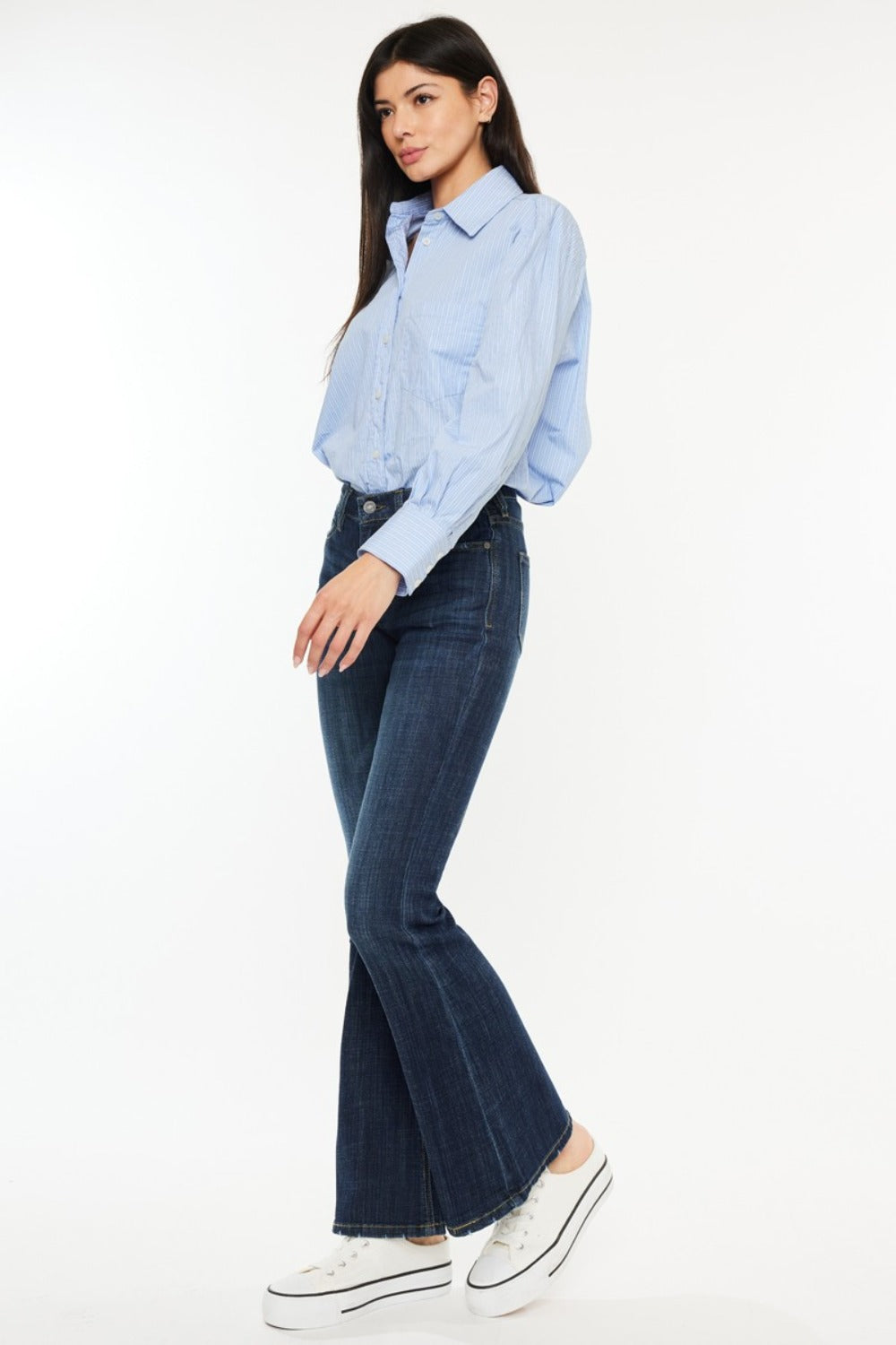 A person poses in a sleeveless brown top, Kancan Full Size Mid Rise Flare Jeans, and sneakers against a plain white background.