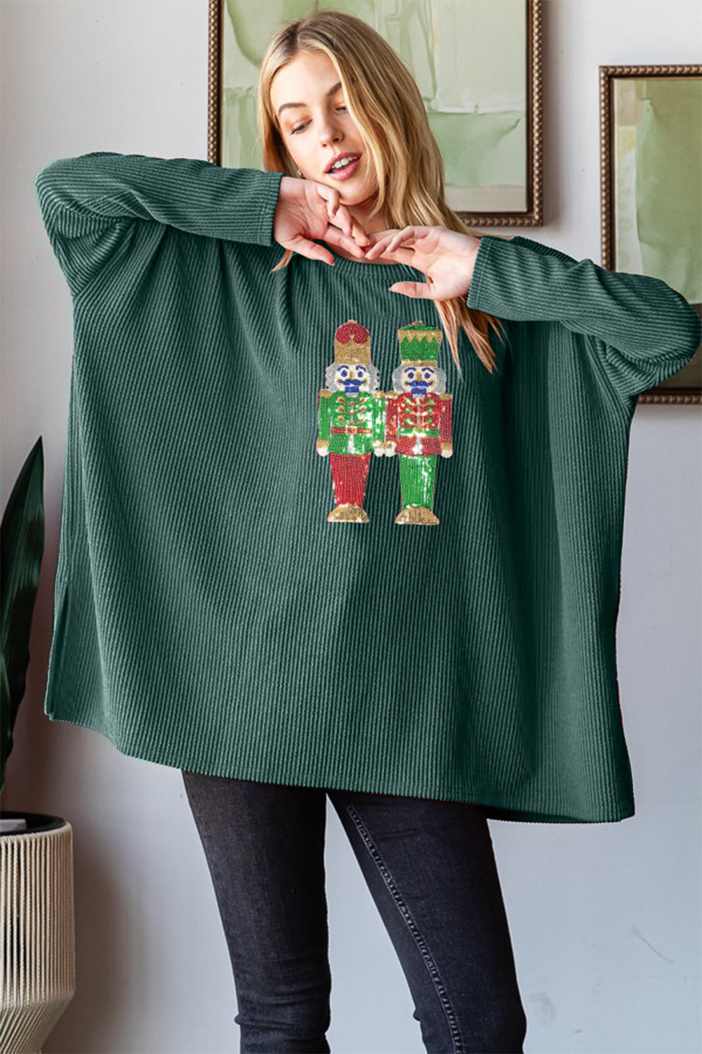 A woman wearing the Heimish Sequin Nutcracker Long Sleeve Ribbed Top smiles while posing indoors, showcasing one of the season's charming holiday outfits.