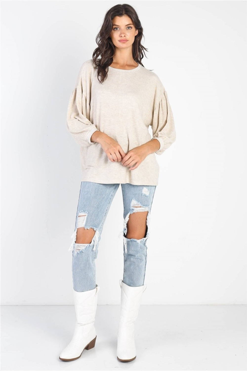 A person with long dark hair stands against a white background, smiling and raising one hand while wearing the trendy and stylish Cherish Apparel Drop Shoulder Puff Sleeve Top in burgundy paired with light blue jeans.