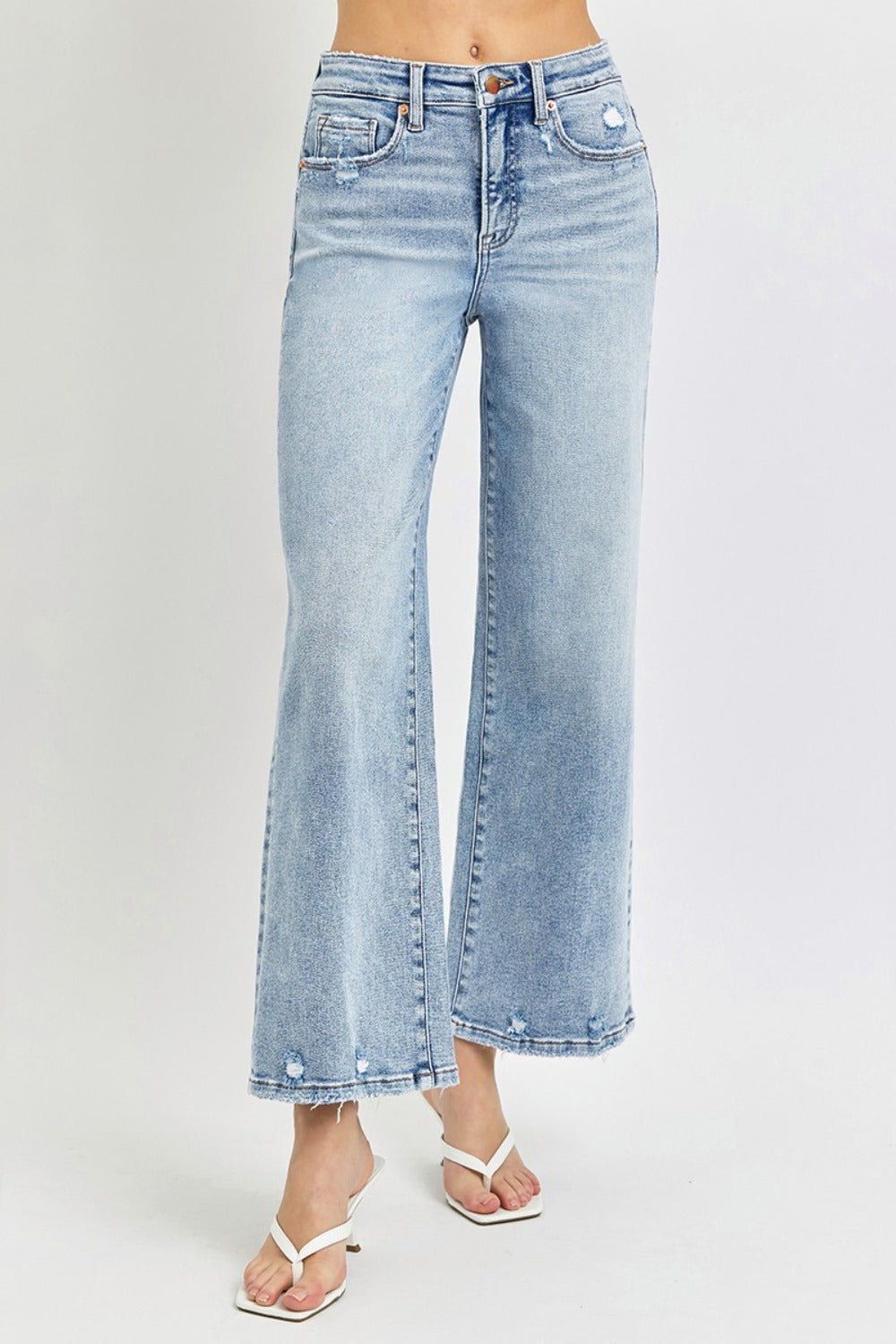 A person wearing RISEN Full Size Tummy Control High Rise Crop Wide Leg Jeans in a light-wash with a frayed hem and white open-toe sandals.