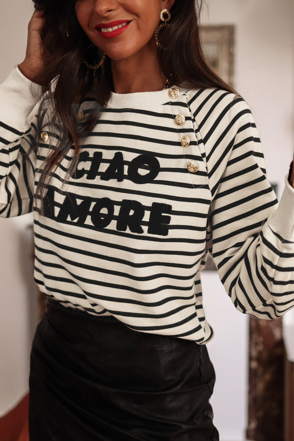 A person with long hair is facing away, wearing a Black Stripe CIAO AMORE Graphic Buttoned Pullover Sweatshirt and a black skirt in an indoor setting. The shirt subtly whispers "CIAO AMORE.