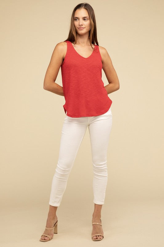 A woman in a stylish and adaptable V Neck Sleeveless Cami Top paired with jeans stands against a beige background. She has long brown hair and maintains a neutral expression.