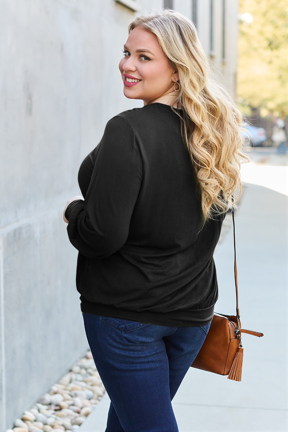 A woman with brown hair is standing against a concrete wall, wearing the Basic Bae Full Size V-Neck Lantern Sleeve Top in teal and blue basic-style jeans, smiling.