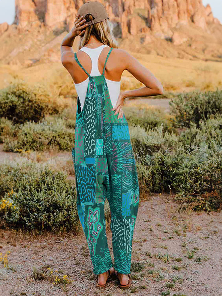 A person standing outdoors in front of rocky terrain, wearing a Full Size Printed V-Neck Sleeveless Jumpsuit and a hat.