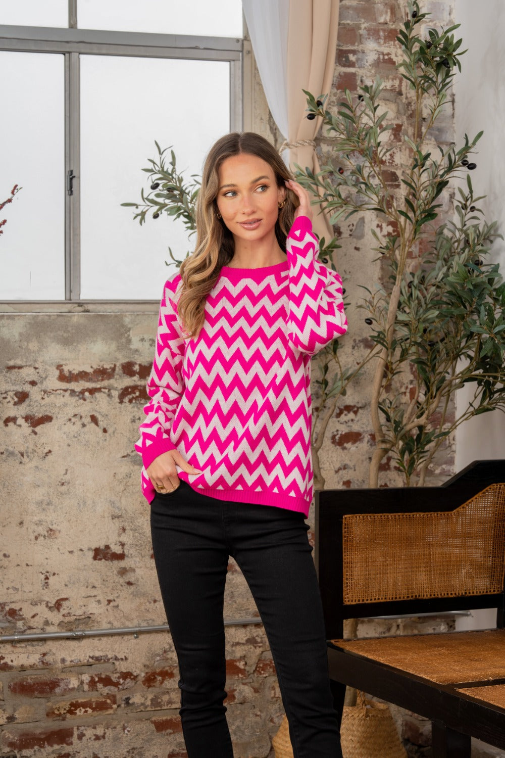 A person wearing the Sew In Love Full Size Wave Stripe Contrast Long Sleeve Sweater stands indoors near a potted plant and a brick wall.