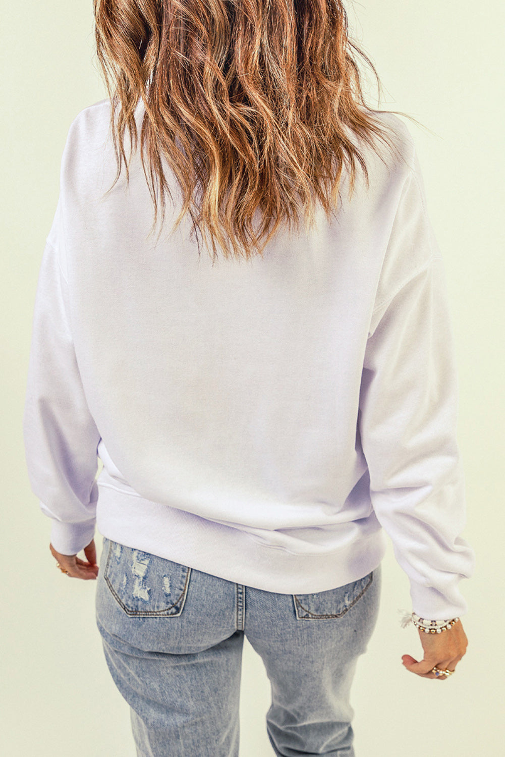 A person wearing a White Oversized Solid Drop Shoulder Sweatshirt and distressed blue jeans is shown from the back, with wavy, shoulder-length hair.