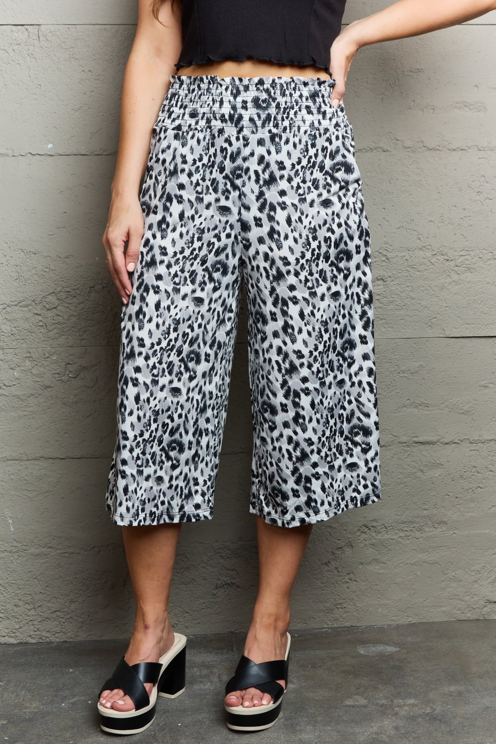 A person wearing Ninexis Leopard High Waist Flowy Wide Leg Pants with Pockets and black platform sandals, standing against a gray wall.