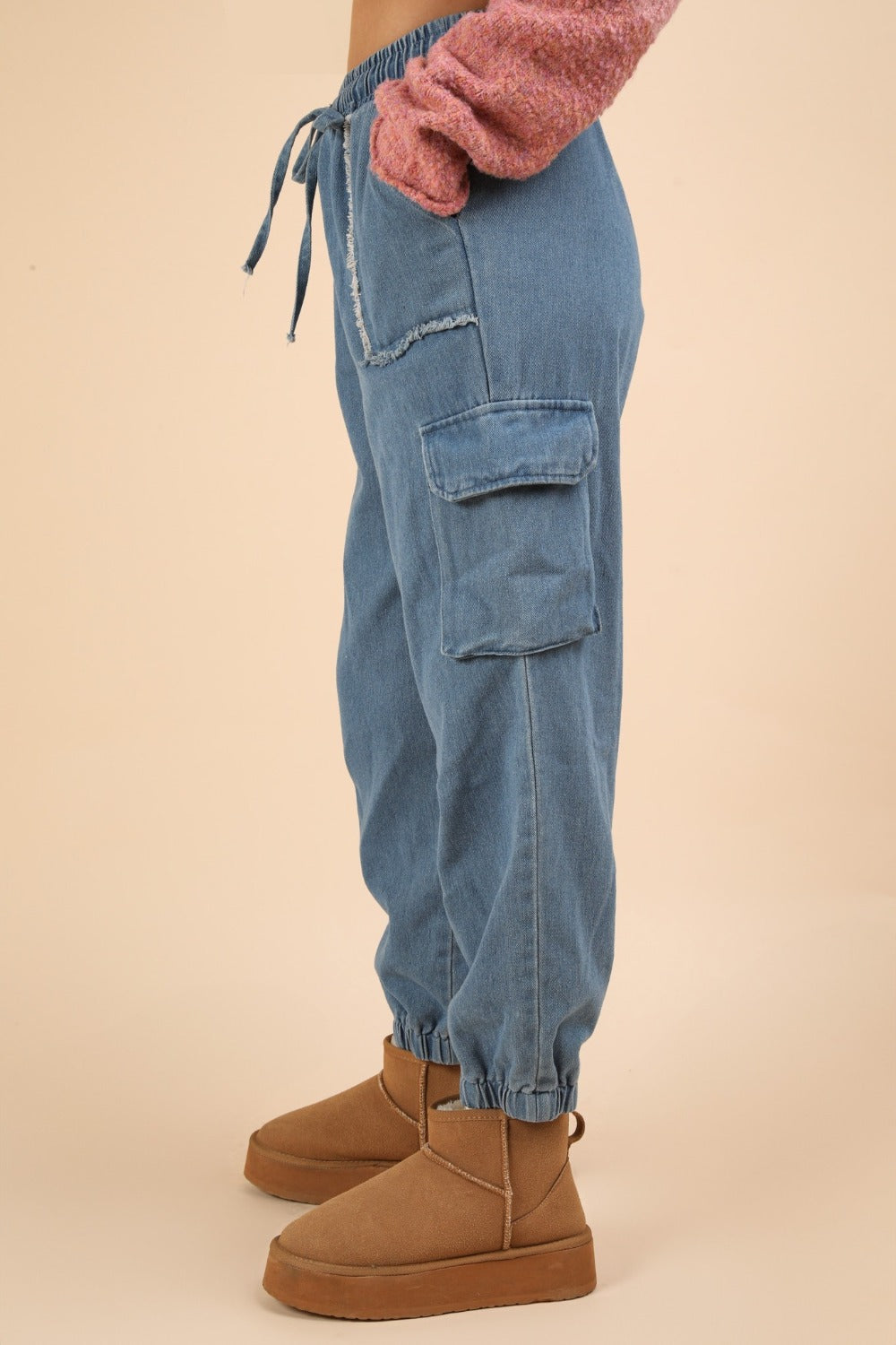 The individual is wearing VERY J Washed Drawstring Jogger Cargo Jeans, which feature elasticated cuffs, large front and side pockets, a drawstring waist, and a fashionable washed finish. They have paired these jeans with tan-colored boots.