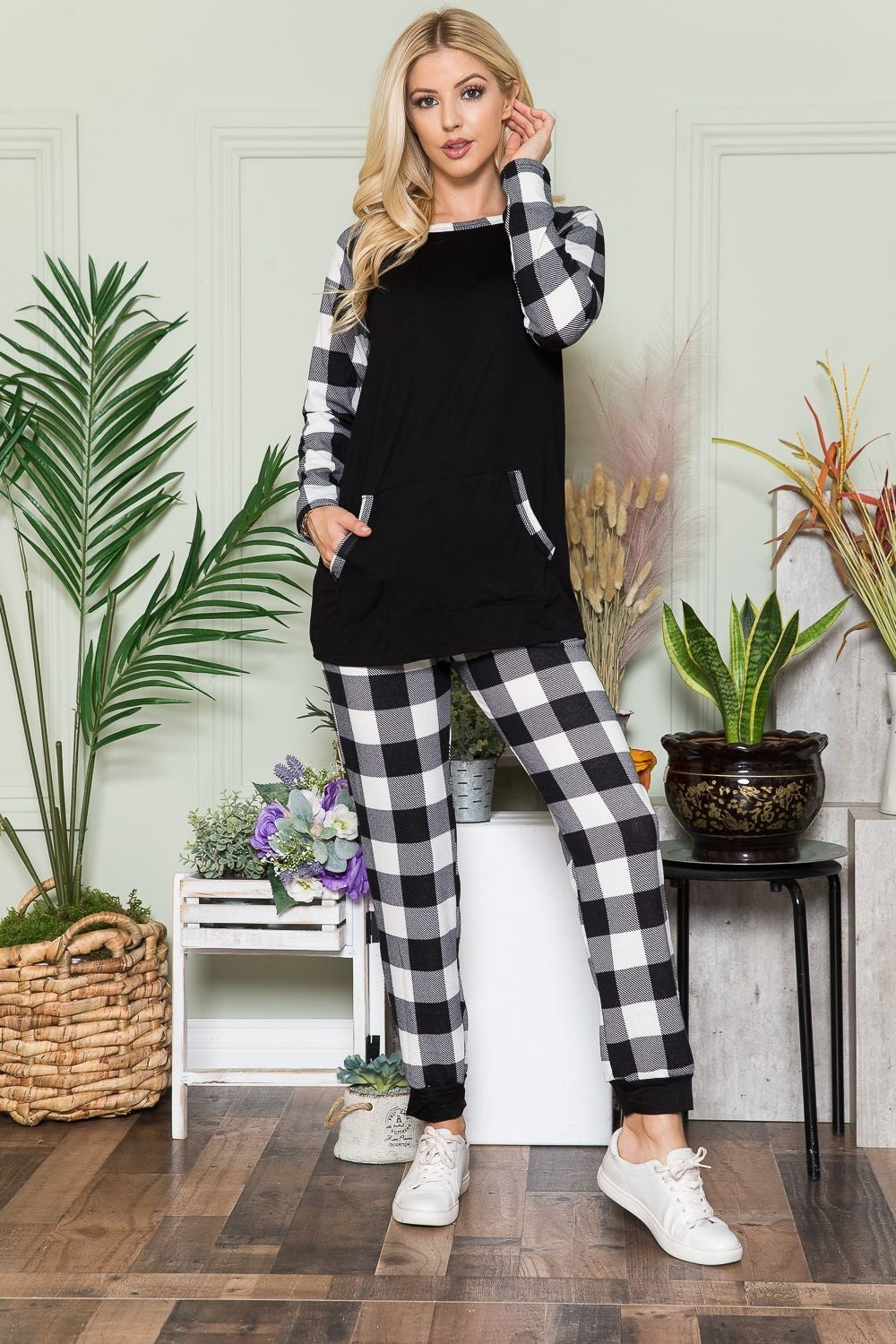 A person wearing the Celeste Plaid Long Sleeve T-Shirt with Pockets stands in a room filled with plants and wooden flooring, presenting a laid-back style.