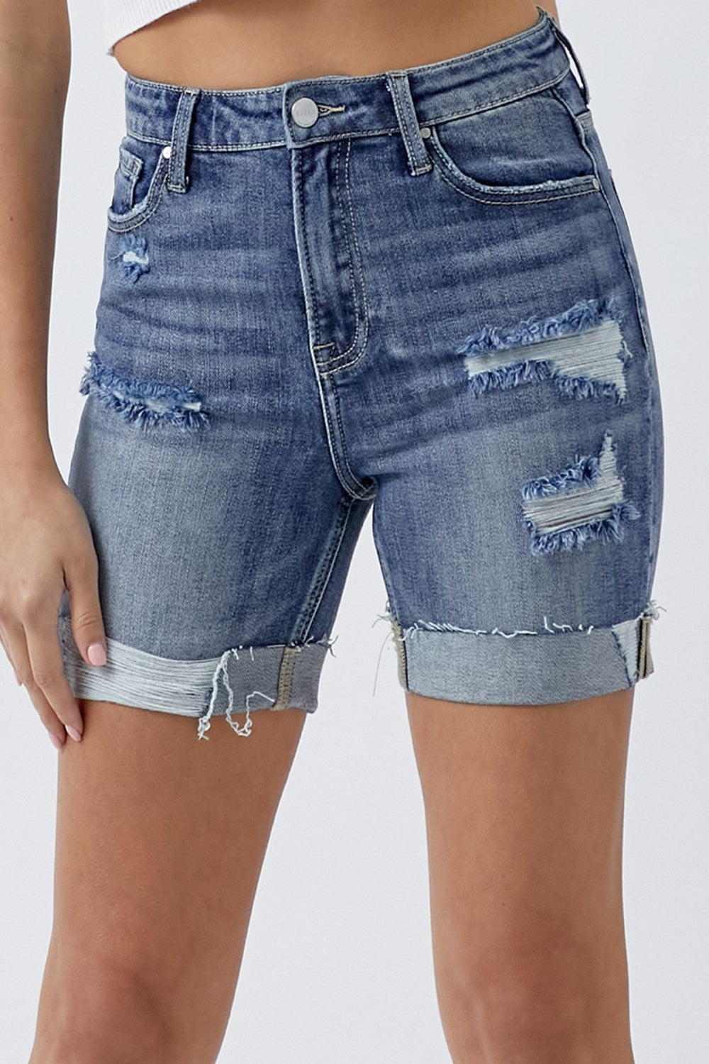 A person is wearing RISEN Full Size Distressed Rolled Denim Shorts with Pockets, characterized by frayed hems and a high waist that perfectly embody the essence of summer wear, standing against a plain background.