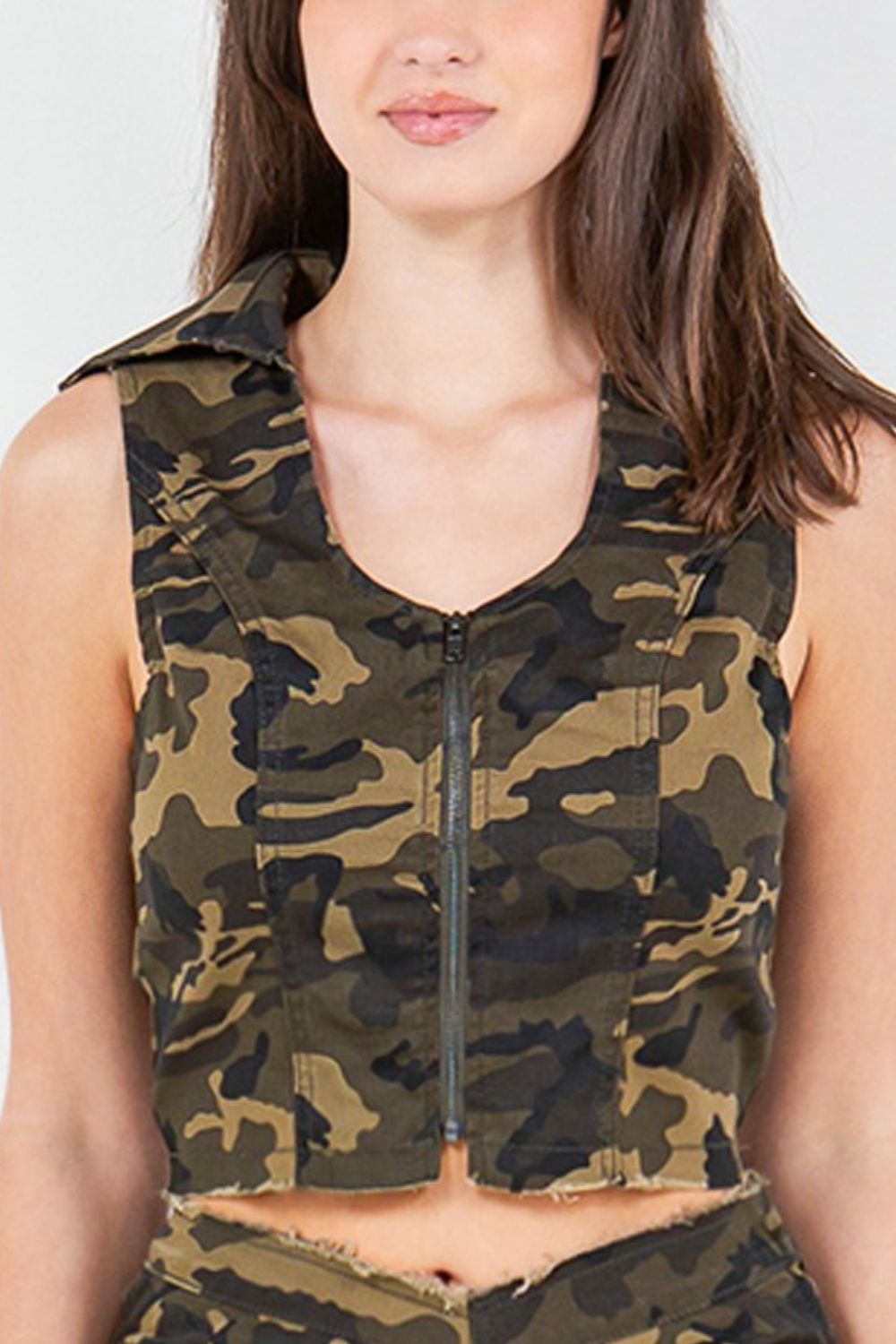 A woman wearing an American Bazi Zip Up Camo Crop Denim Vest and camouflage pants stands against a plain white background, showcasing an urban chic style that's perfect for a trendy and edgy wardrobe.