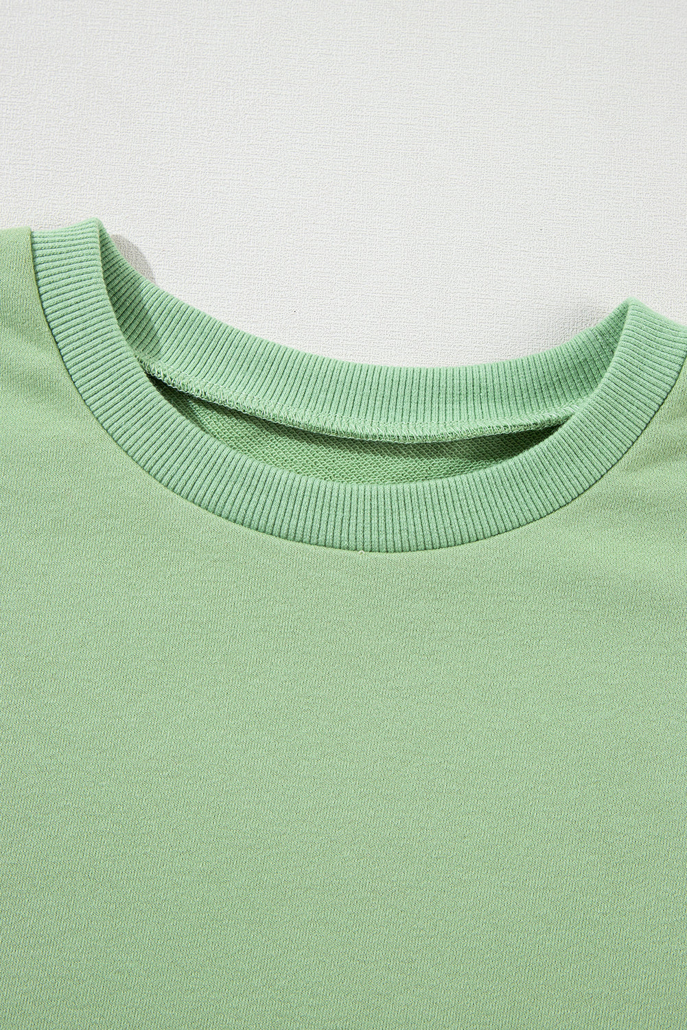 A person with long hair, seen from the back, wearing a Grass Green Solid Fleece Lined Drop Shoulder High Low Sweatshirt and black pants.