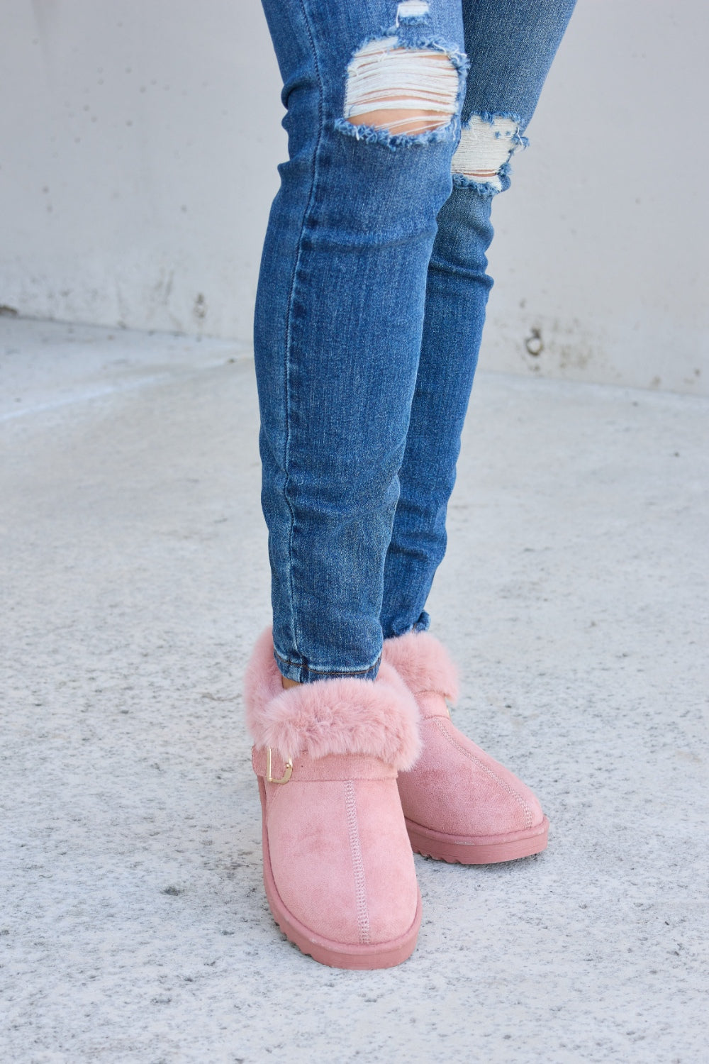 A person stands on a concrete surface, sporting ripped blue jeans and the Forever Link Furry Chunky Thermal Ankle Boots. The furry lining of these fashionable boots suggests both comfort and warmth for winter.