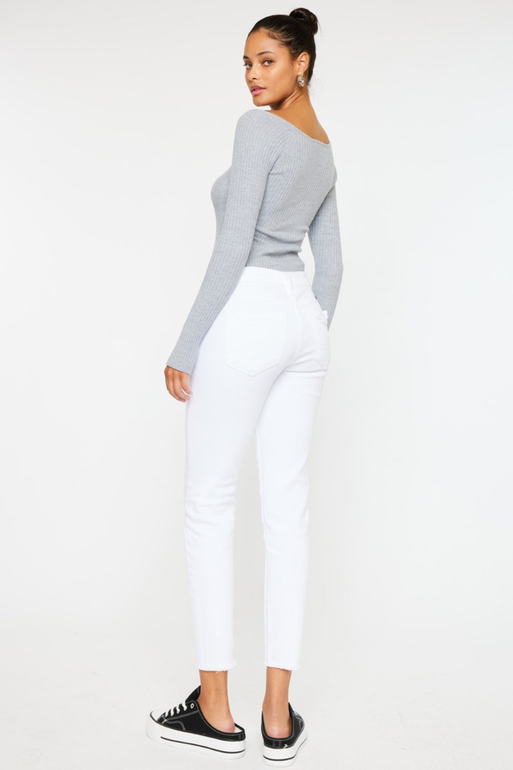 A person models a versatile gray long-sleeve top paired with flattering fit Kancan Mid Rise Ankle Skinny Jeans and sleek black sneakers, all set against a pristine white background.