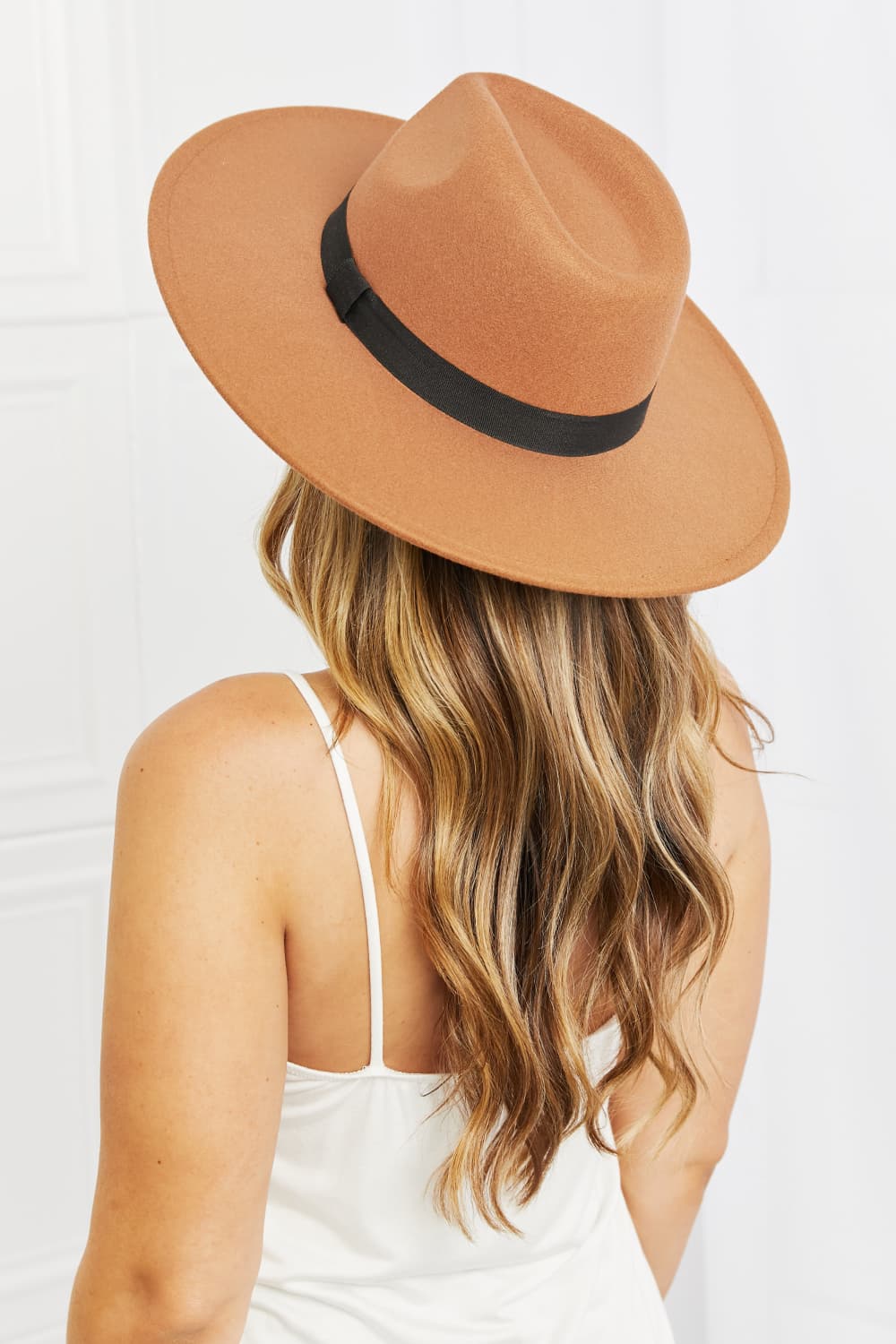 A woman with long blonde hair in a white lace-trimmed top smiles and looks down while wearing the Fame Enjoy The Simple Things Fedora Hat, a tan fedora featuring a black band and crafted from high-quality materials.