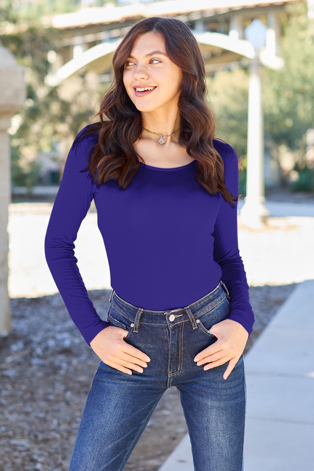 A person poses confidently in the Basic Bae Full Size Round Neck Long Sleeve Bodysuit, made from a rayon spandex blend, with one hand touching their neck and the other resting on their hip.