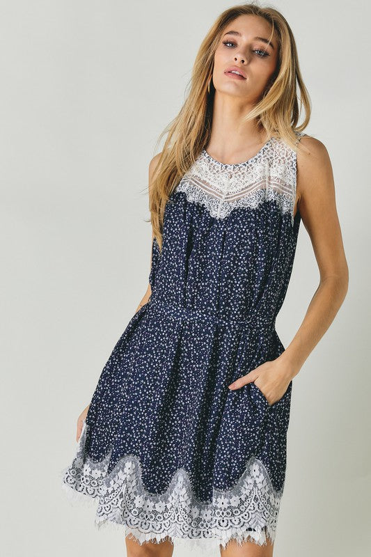 A woman wearing the Printed Sleeveless Lace Trim Mini Dress is seated against a light background.