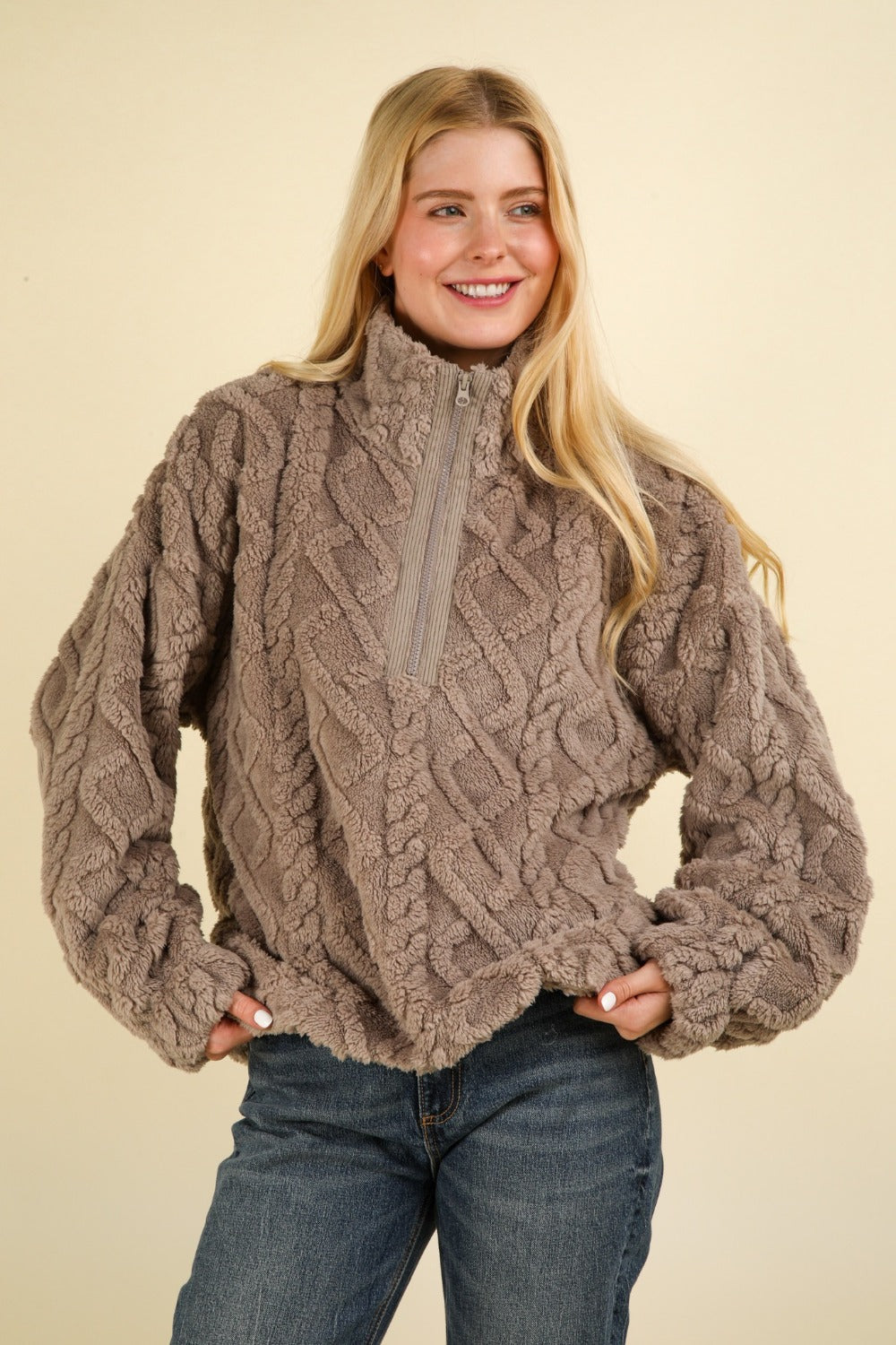 A person smiling and wearing the VERY J Fuzzy Fleece Half Zip Cable Pattern Sweatshirt in gray, along with blue jeans.